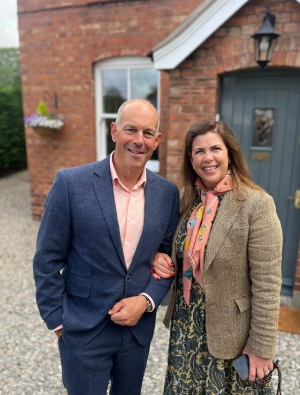 Phil Spencer in a blue suit and peach shirt standing with Kirstie Allsopp in a brown outfit and peach scarf