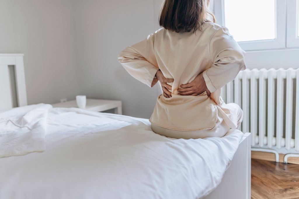 Cropped Image of Senior Woman Suffering From Backache in Morning Sitting on Bed, Panorama With Free Space. Lower Back Pain in Elderly Person. Woman Feels Back Pain Massaging Aching Muscles. Mature Woman Feeling Morning Discomfort in Aching Back in the Bedroom.