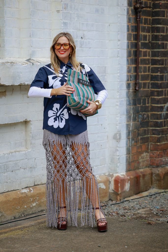 A guest wearing yellow tinted sunglasses, navy Hawaiian shirt, Marni stripped green bag, Wynn Hamlyn fringed maxi skirt during Australian Fashion Week 2025 on May 15, 2025 in Sydney, Australia