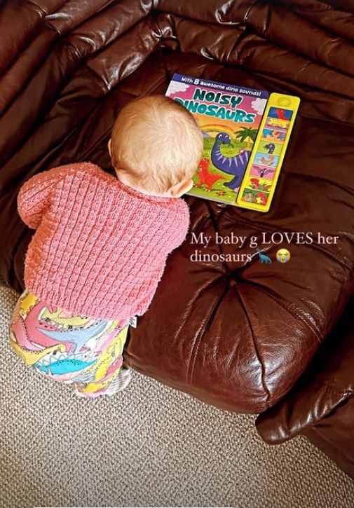 A baby climbing on a sofa with the book Noisy Dinosaurs