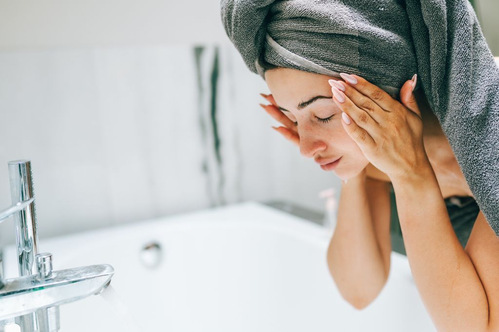 woman in bath towel washes face early morning. 