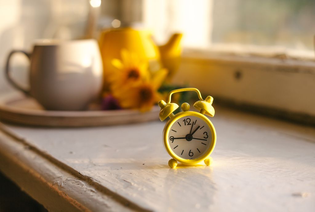 Fall seasonal still life. Retro alarm clock. Fall back concept. Cup with autumn flowers and kettle on wooden tray on window sill