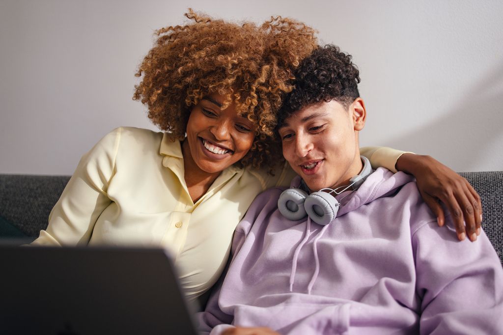 woman sitting with teenage son on the sofa at home using a laptop 