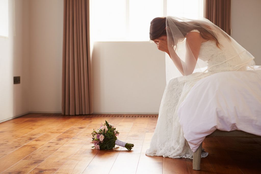 Bride sitting on the bed with her head in her hands and her flowers on the floor