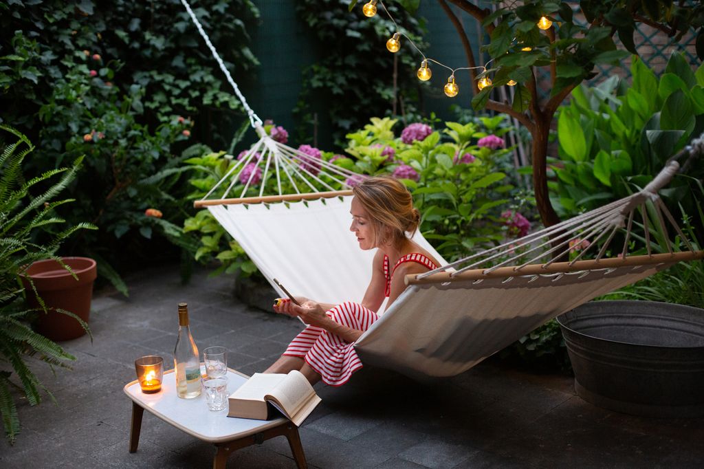 Woman relaxing in hammock in her garden, looking at smartphone