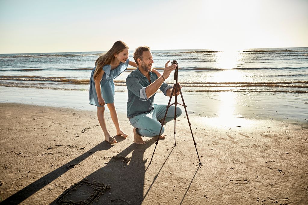 Father and daughter preparing a tripod for a a photo on the beach