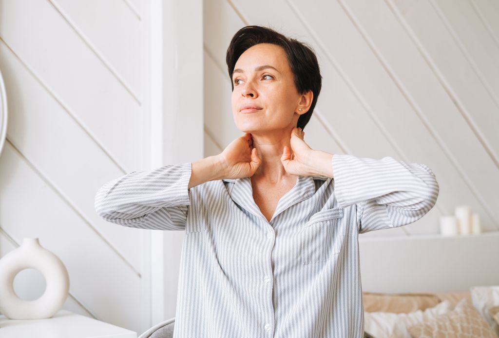 Portrait of young adult brunette woman doing facial massage with hands in bedroom at home, morning skincare routine