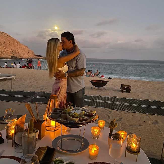 Josh and Christina kissing and embracing on a beach at sunset