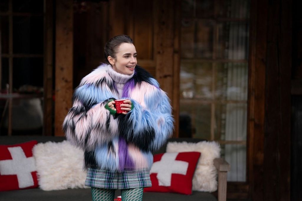 Lily Collins in a fur jacket holding a red mug