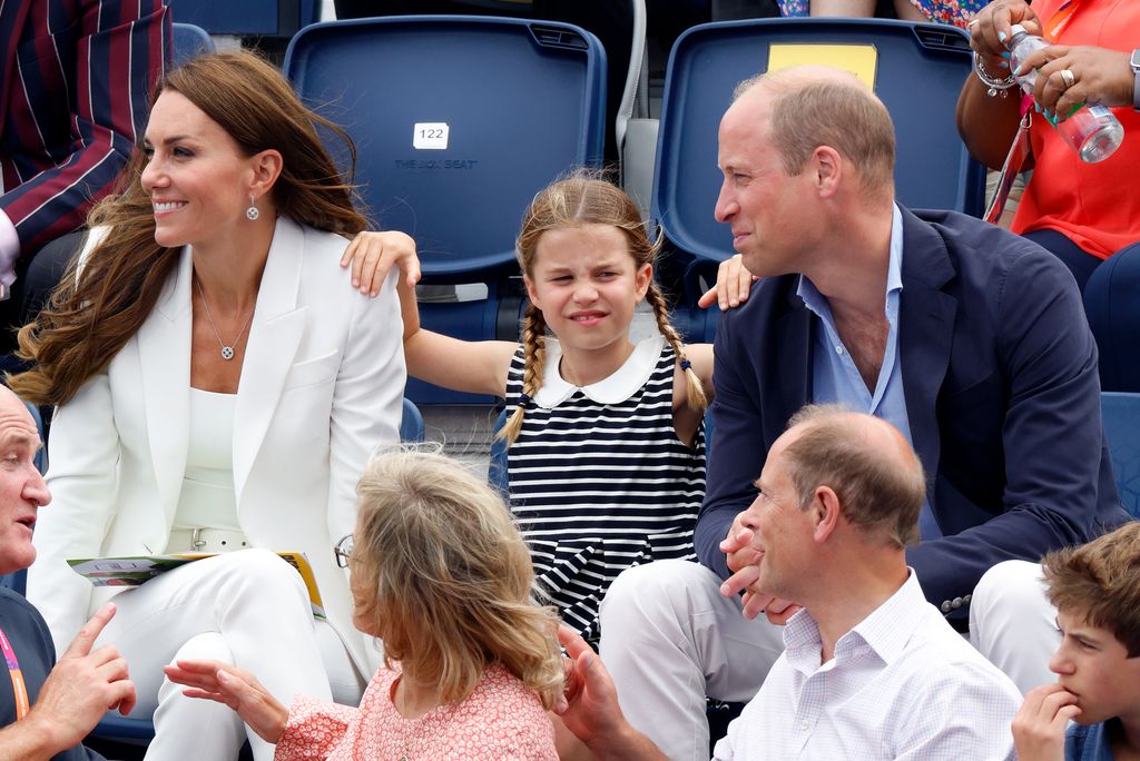 Charlotte sitting in between kate and william, a hand on each of their shoulders 