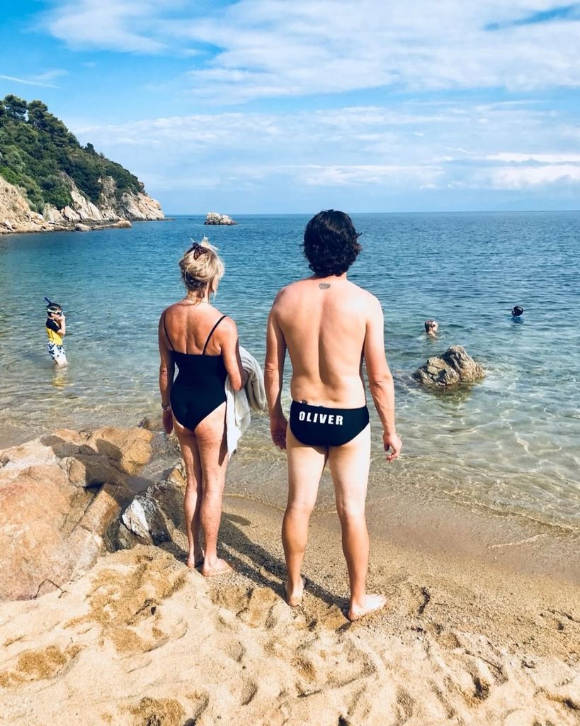 Goldie and Oliver on the beach in their swimwear while his kids swim in the water