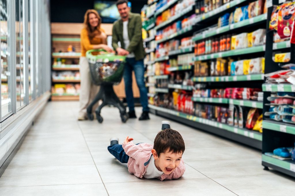Shot of small boy lying on floor crying while his mum and dad shop for groceries