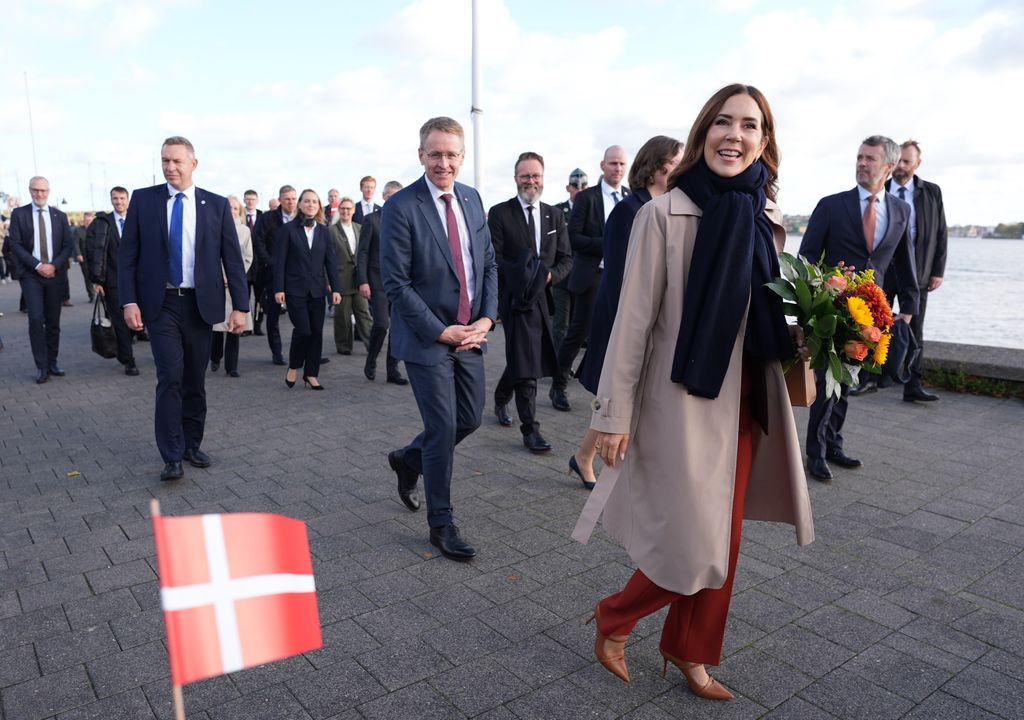 Queen Mary walking on pier in a trench coat over her outfit