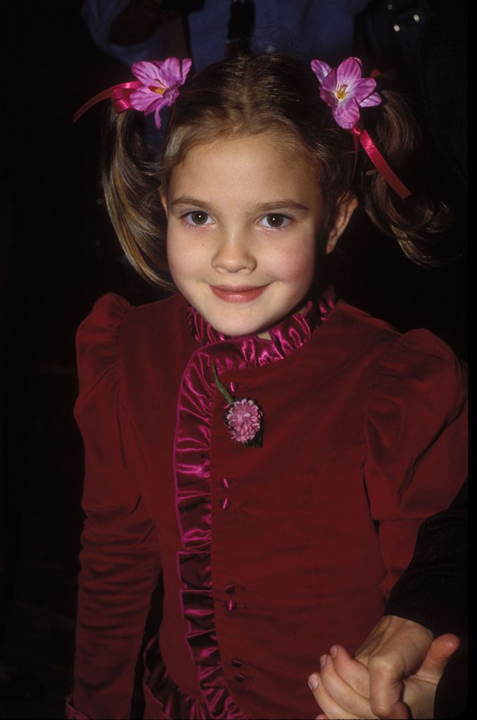 A young Drew Barrymore in a red dress with floral hairpins