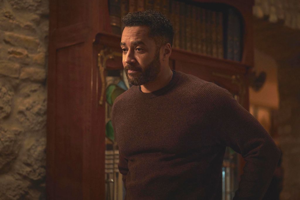 man in brown jumper standing in front of book case