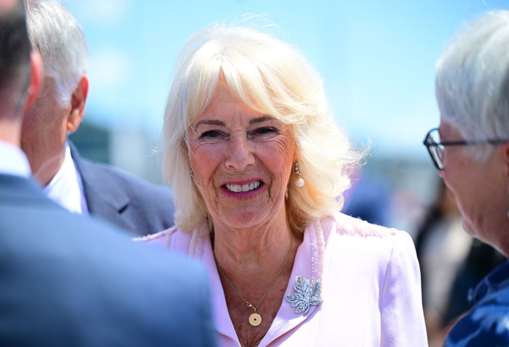 Queen Camilla smiling a pink dress with a diamond brooch