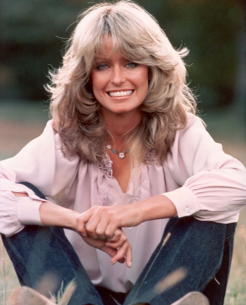 Publicity portrait of American actor and model Farrah Fawcett smiling while sitting outdoors in blue jeans and a mauve blouse.   (Photo by Hulton Archive/Getty Images)