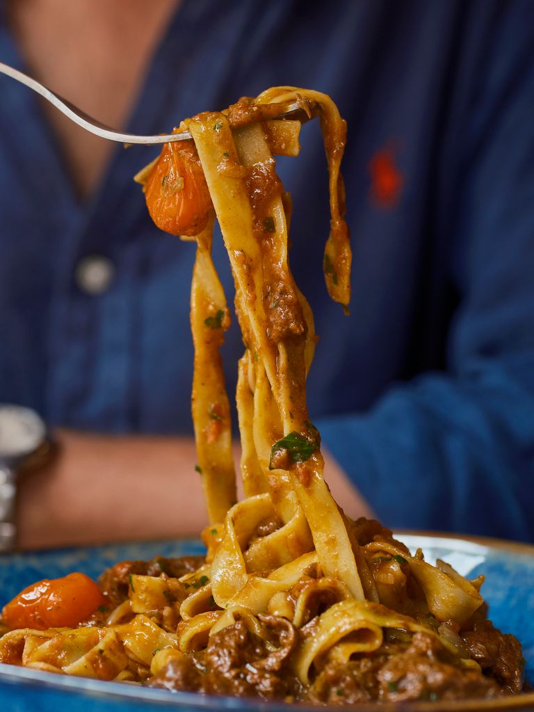 A man in blue uniform holding a fork with pasta coming off it