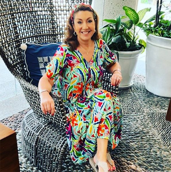 Jane McDonald sat in a chair wearing a brightly coloured dress