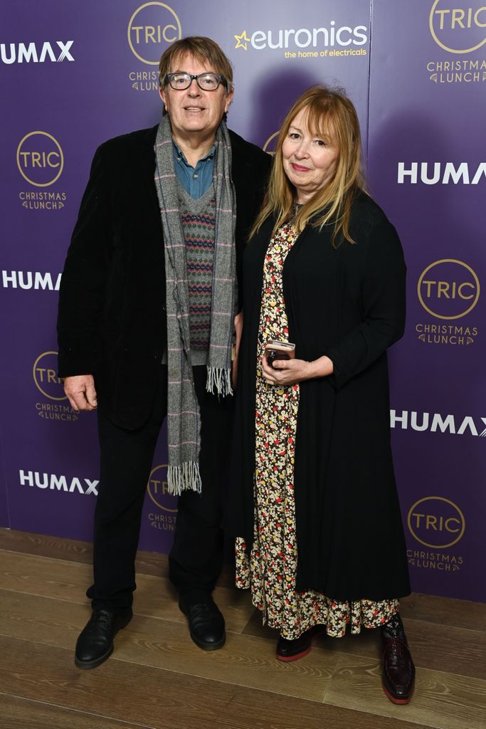 Giles Wood in a jacket and grey scarf and Mary Killen in a floral dress