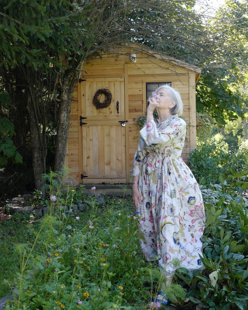 Woman smelling flowers in a garden in front of a shed 