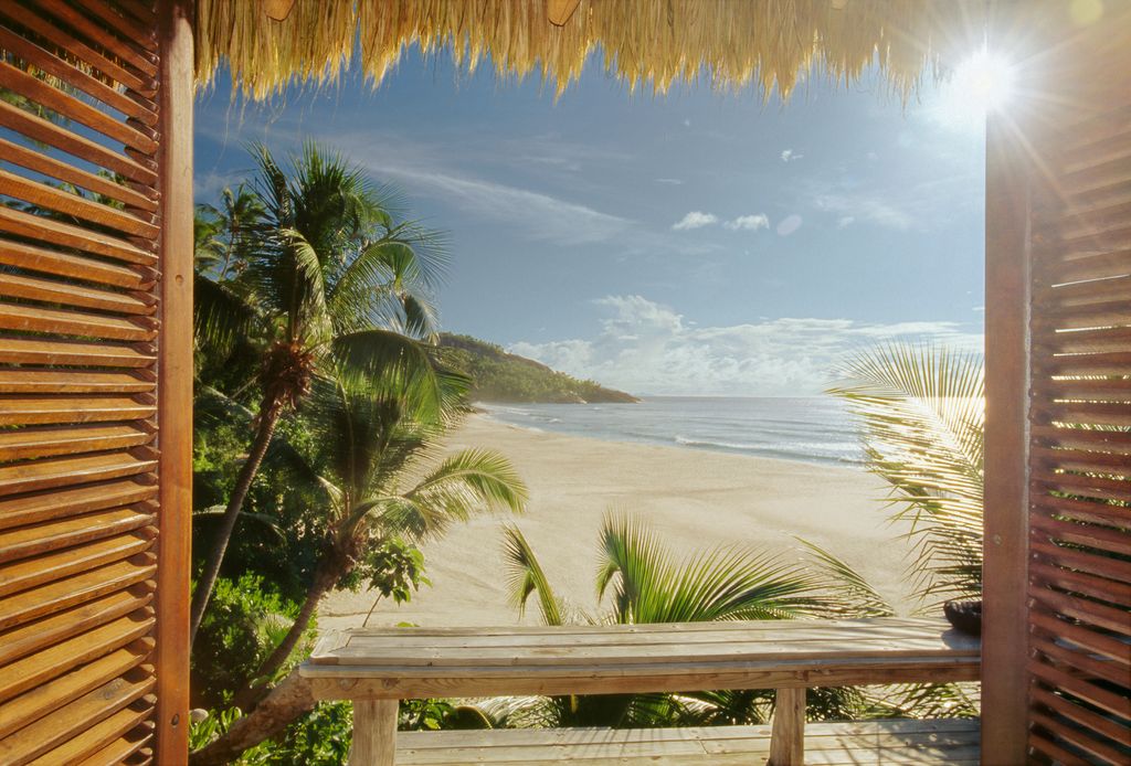 Window with wooden shutters opening on a wild white tropical beach