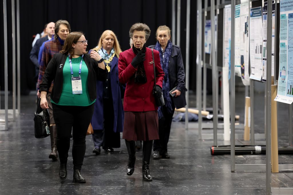La princesse royale marchant en groupe de personnes en blazer et jupe cramoisi 