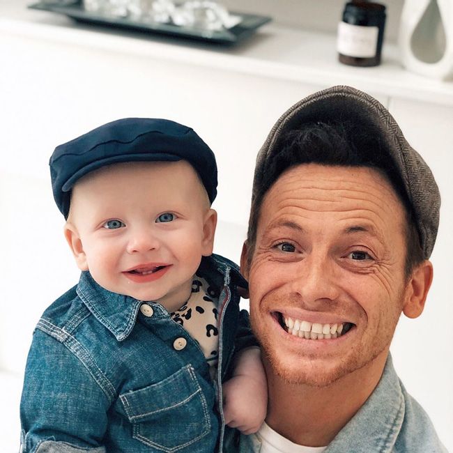 a baby and a man smile broadly at the camera whilst wearing matching flat caps