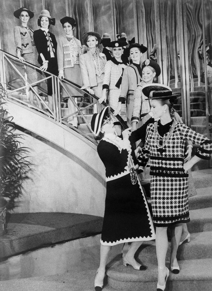 The lady looking over the long-legged lovelies is Coco Chanel who has designed their clothes. The popular French designer is portrayed by Katharine Hepburn in the musical Coco.