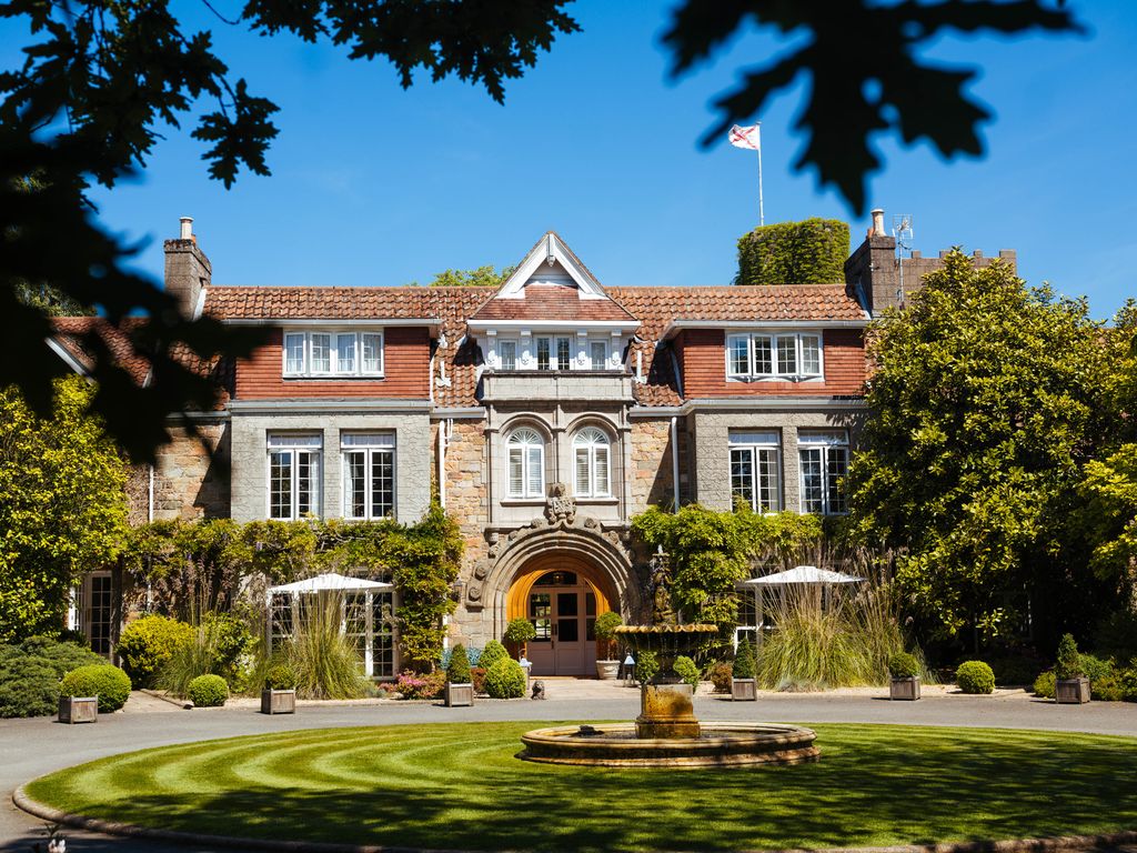 Front of a manor house with a circular drive under blue skies