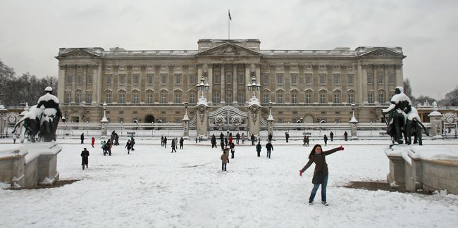 Buckingham Palace in the snow with people playing in front of it 