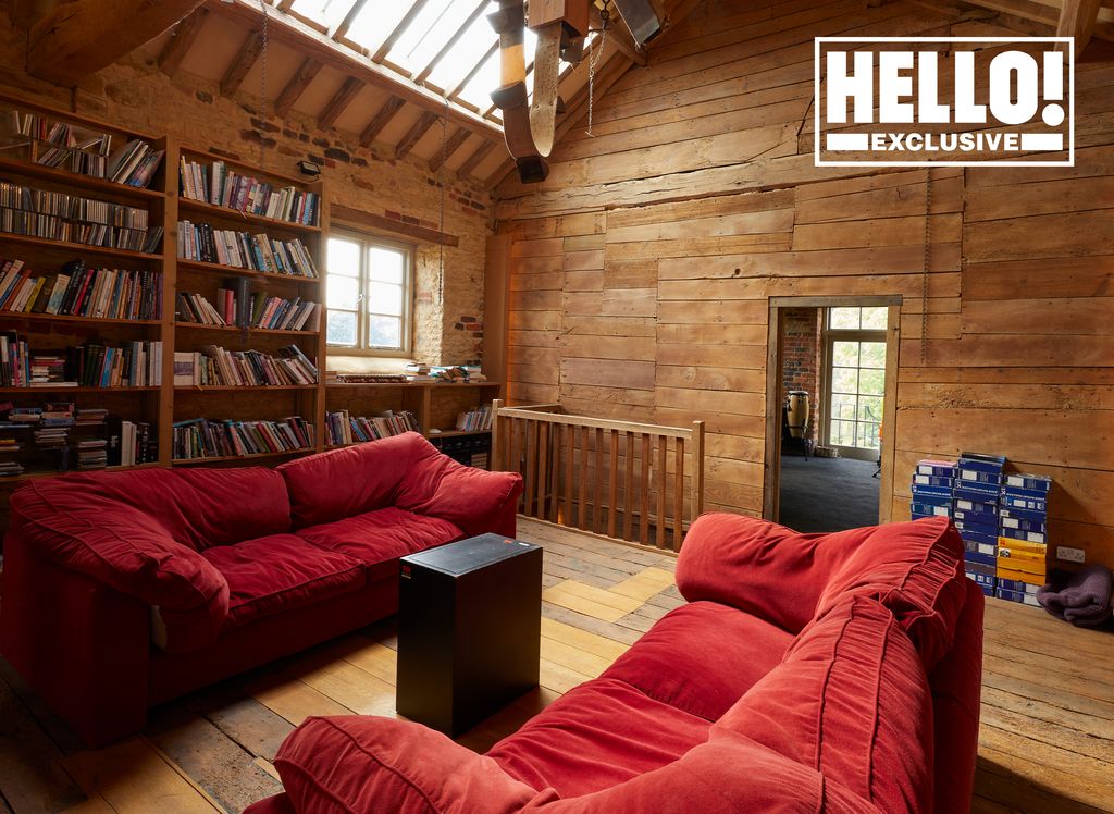 Blur star Alex James's library room at farmhouse in Kingham, Oxfordshire featuring wood panelled walls and red sofas  