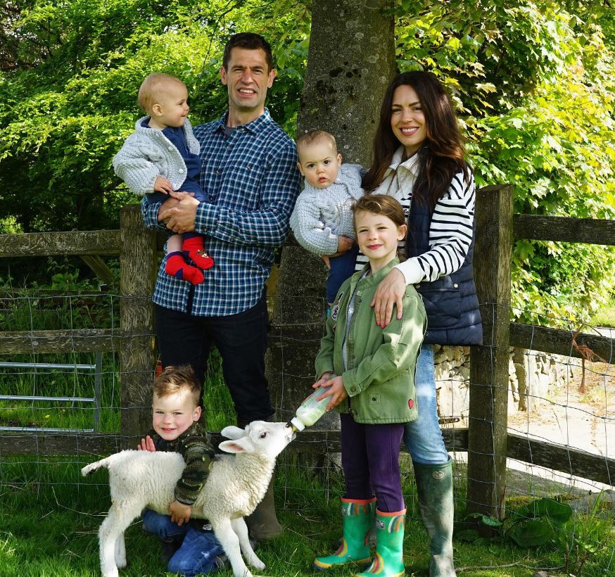 A family of six, with two young children bottle-feeding a lamb