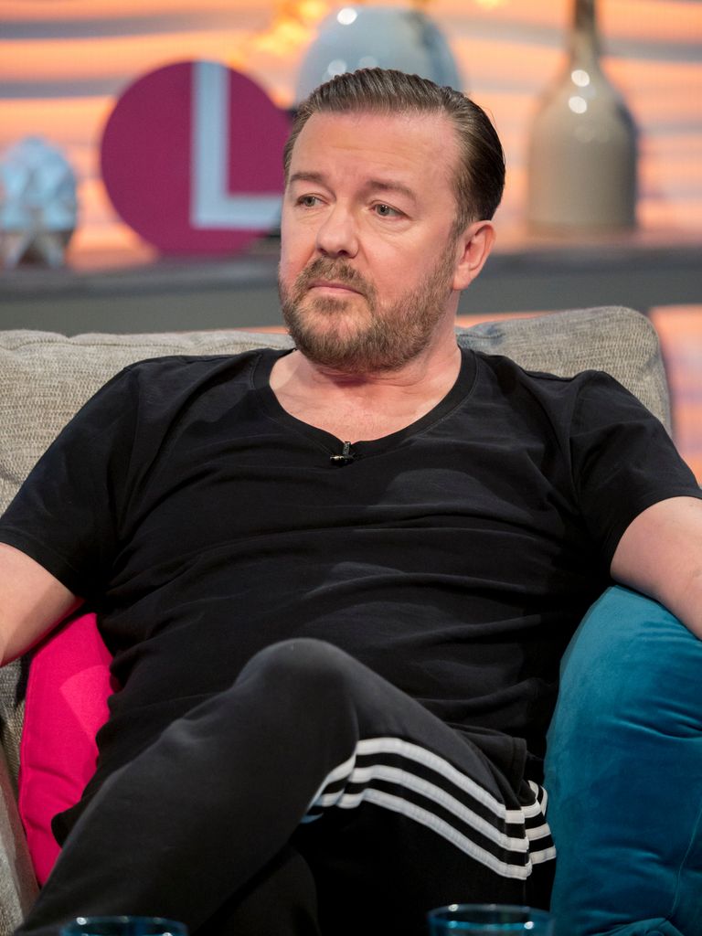 Ricky Gervais looking sad in a black shirt and tracksuit bottoms