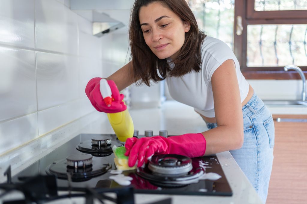 A woman Cleaning Gas Stove With Sponge At Kitchen
