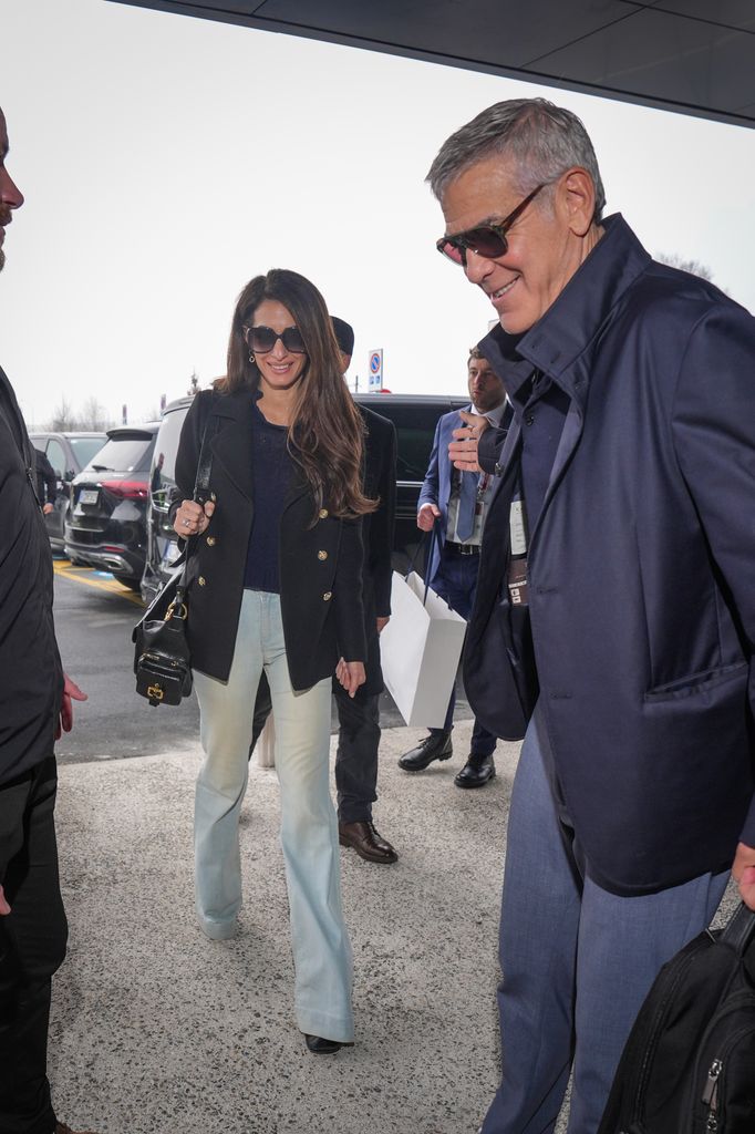 Amal Clooney en jean évasé avec George entrant dans l'aéroport