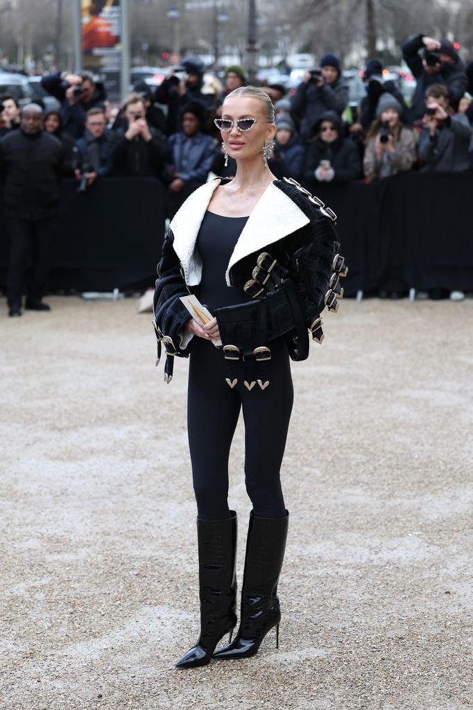 Tatiana Korsakova's edgy outfit featured a black bodysuit with a cropped jacket covered in silver buckles, thigh-high stiletto boots, and statement sunglasses, serving futuristic couture-meets-street-style vibes.