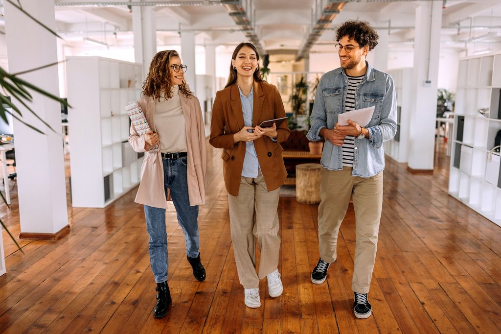 Group of smiling young colleagues walking and talking in modern office
