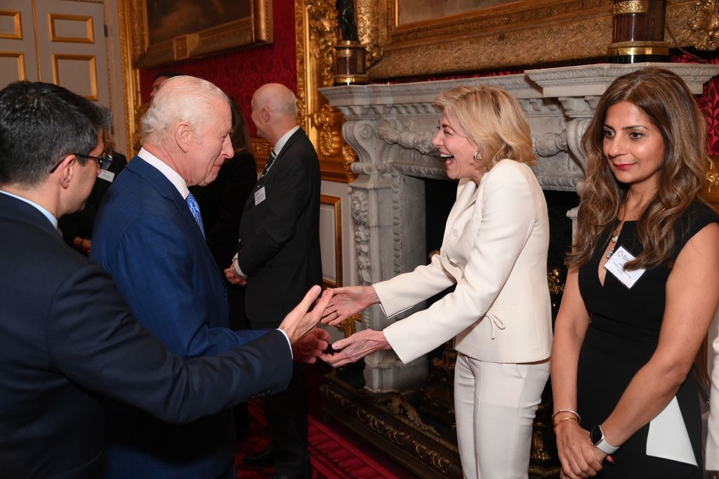 King Charles shaking hands with a woman in a white outfit