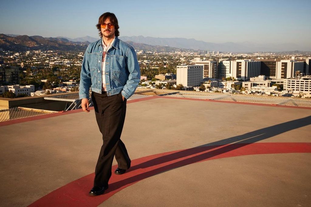 Lucas Bravo walks across rooftop in LA wearing denim jacket in promo shot