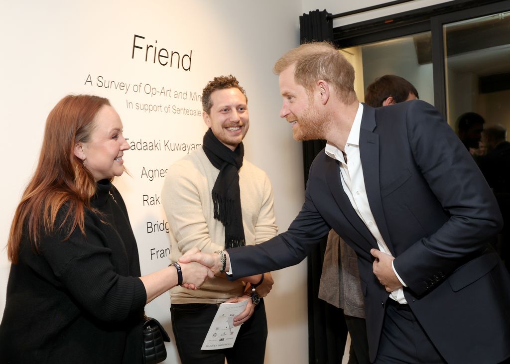 Prince Harry in a grey suit shaking hands with a woman