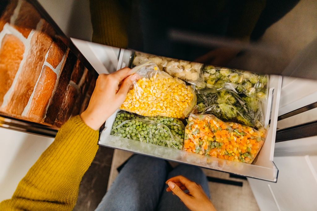 Woman putting container with frozen mixed vegetables to refrigerator