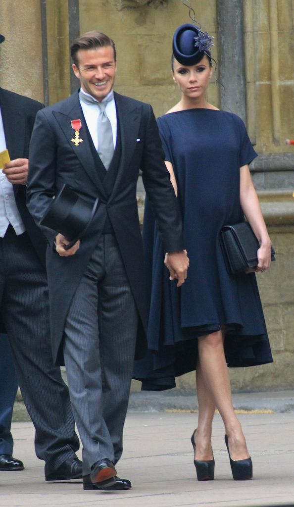 David and Victoria Beckham outside Westminster Abbey. David is wearing a morning suit with medallion on his label. He is carrying a top hat. 