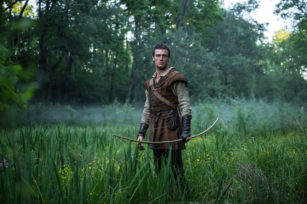 man standing in field of grass holding bow and arrow