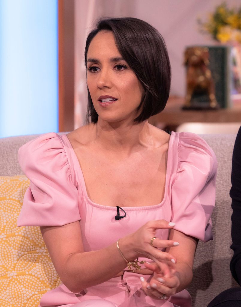 Janette Manrara sitting on a sofa in a pink dress