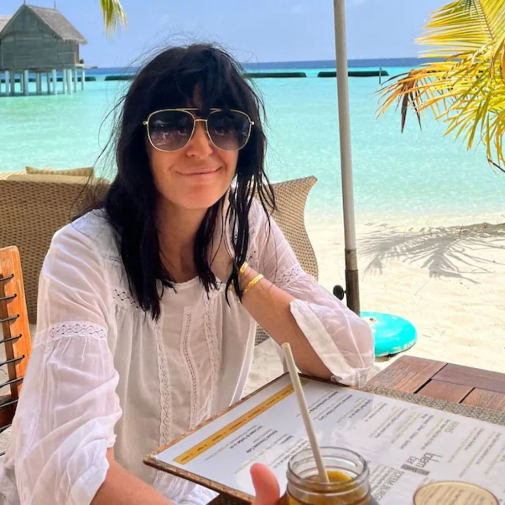 Claudia Winkleman in a white top with wavy hair on the beach