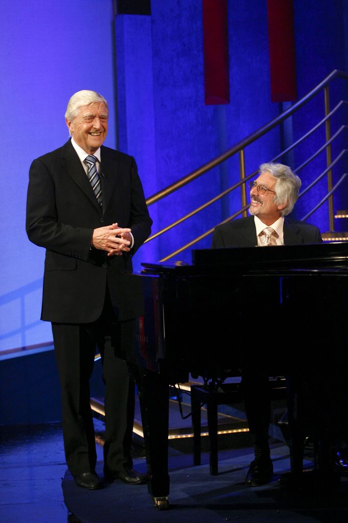 Sir Michael Parkinson de pie mientras Laurence Holloway se sienta al piano