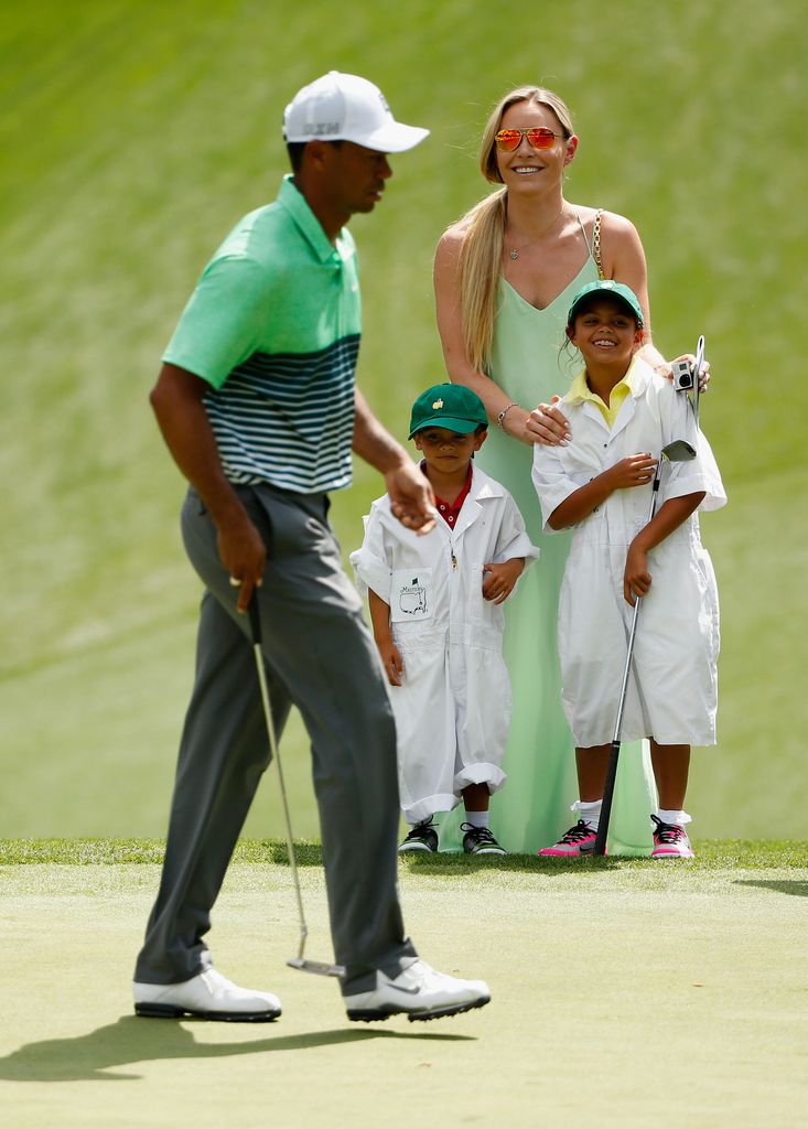 Tiger Woods of the United States walks across a green as his girlfriend Lindsey Vonn, son Charlie and daughter Sam look on during the Par 3 Contest prior to the start of the 2015 Masters Tournament