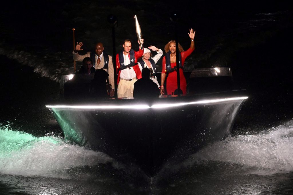 Rafael Nadal (2L) holds the Olympic torch next to US' athlete Carl Lewis (L), Romanian gymnast Nadia Comaneci (2R) and US tennis player Serena Williams (R) on the river Seine 