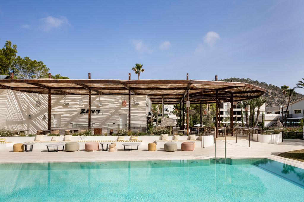 The Zayt restaurant at Kimpton Aysla Mallorca, showcasing an inviting outdoor dining area with rustic wooden beams and chic seating arrangements beside a serene pool.